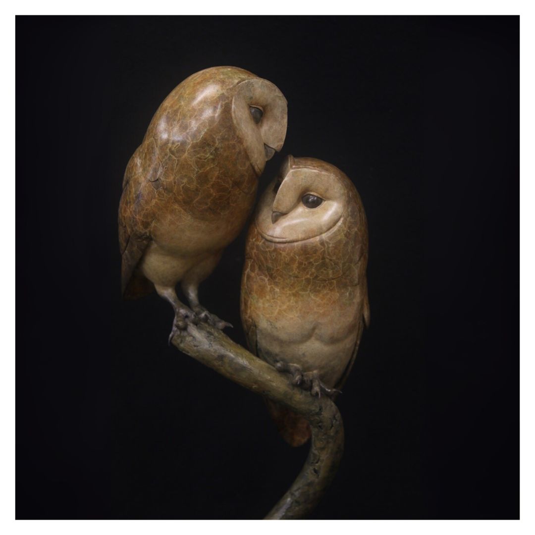 Two owl sculptures on a branch against a black background