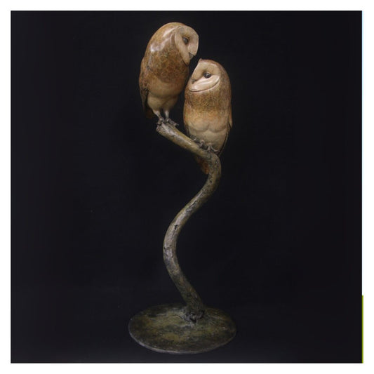 Bronze sculpture of two owls on a branch against a black background