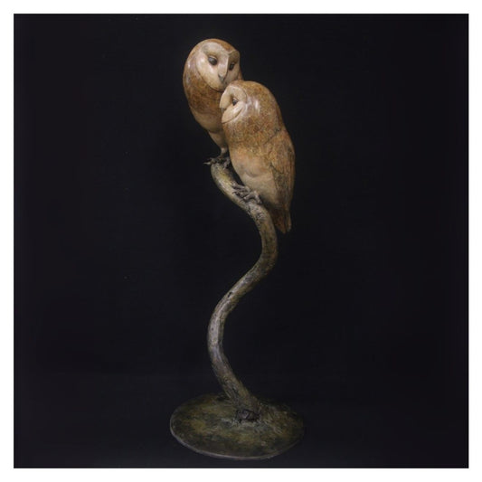 Bronze sculpture of two owls perched on a branch against a black background