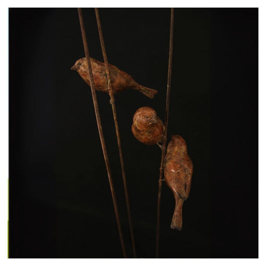 Two rusted metal birds perched on thin rods against a black background