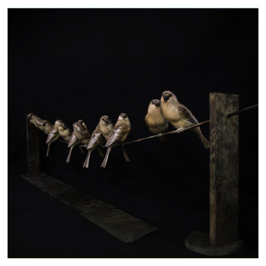 Statue of birds perched on a wire against a dark background