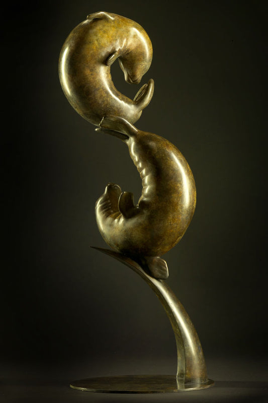 Bronze sculpture of two seals in a dynamic pose against a dark background