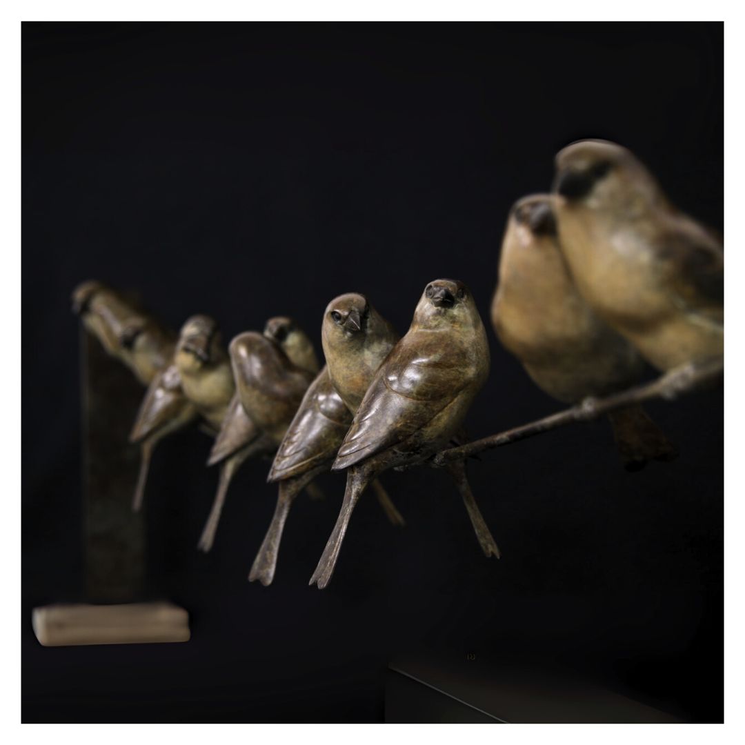 Bronze birds perched on a branch against a dark background
