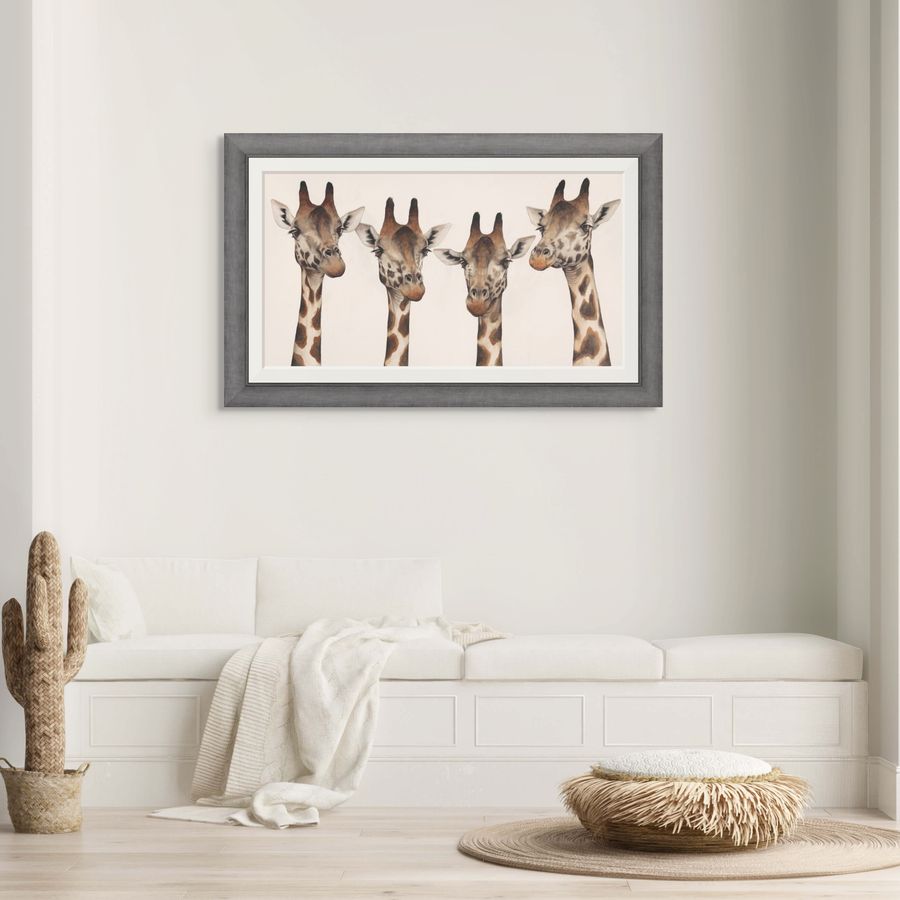 Framed artwork of four giraffes on a wall above a white sofa.